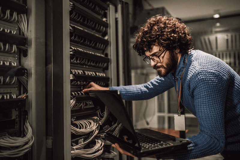 Engineer plugging cables into a server while looking at a laptop.